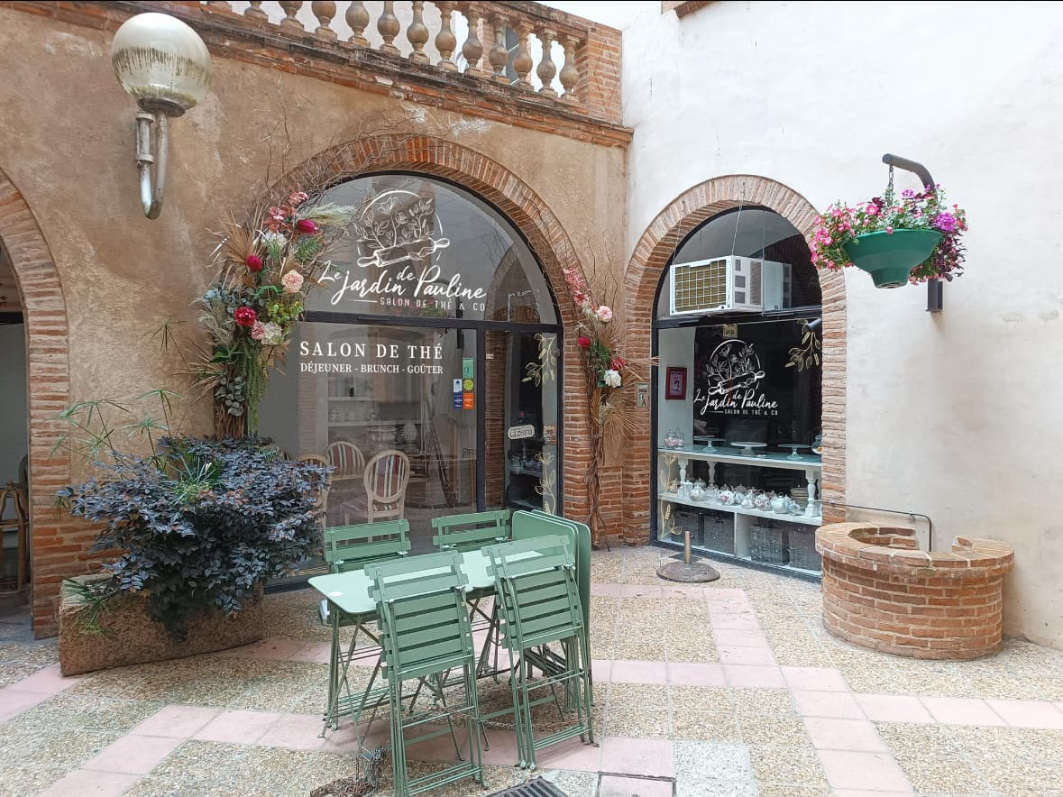 La terrasse fleurie du Jardin de Pauline, ses chaises vertes et les arches du Passage du Vieux Palais